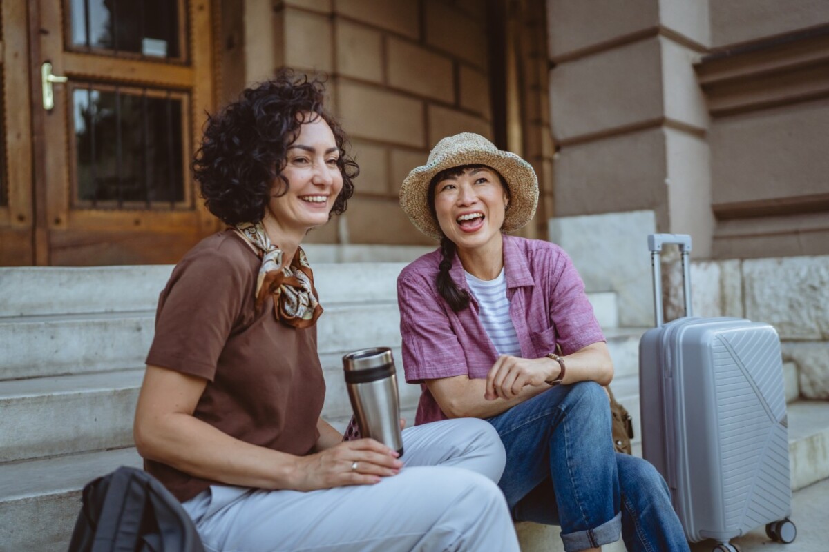 A tourist with a suitcase chats on stone steps with a local woman, using simple Japanese phrases to break the ice at the start of a trip.